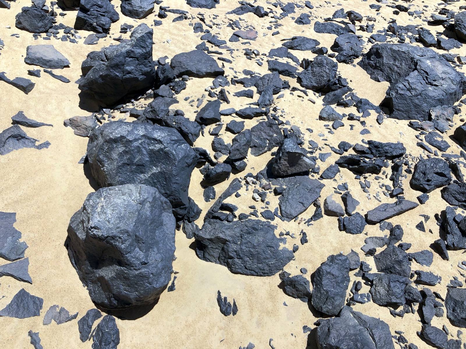 Black basalt and ironstone fragments strewn over golden sand