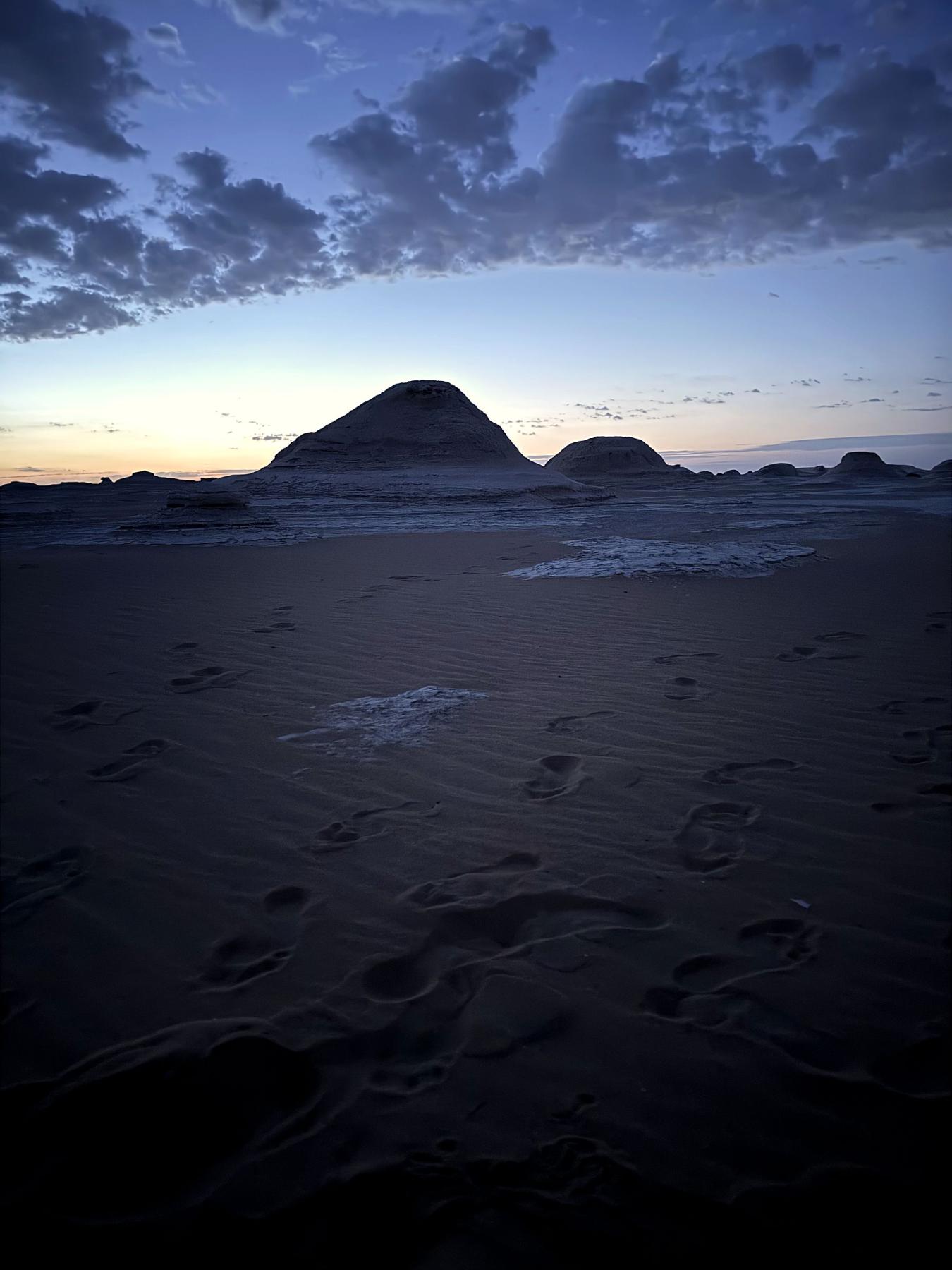 Desert formations silhouetted at twilight with footprints in the sand