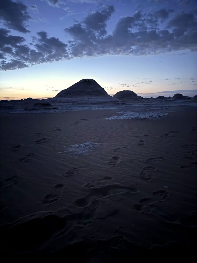 Desert formations silhouetted at twilight with footprints in the sand