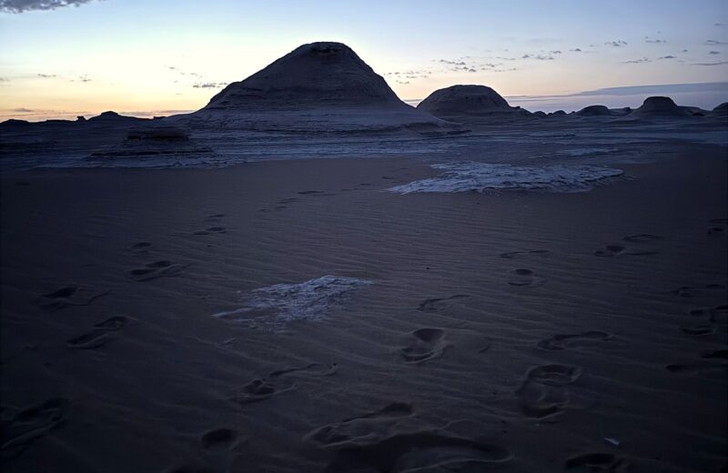 Desert formations silhouetted at twilight with footprints in the sand